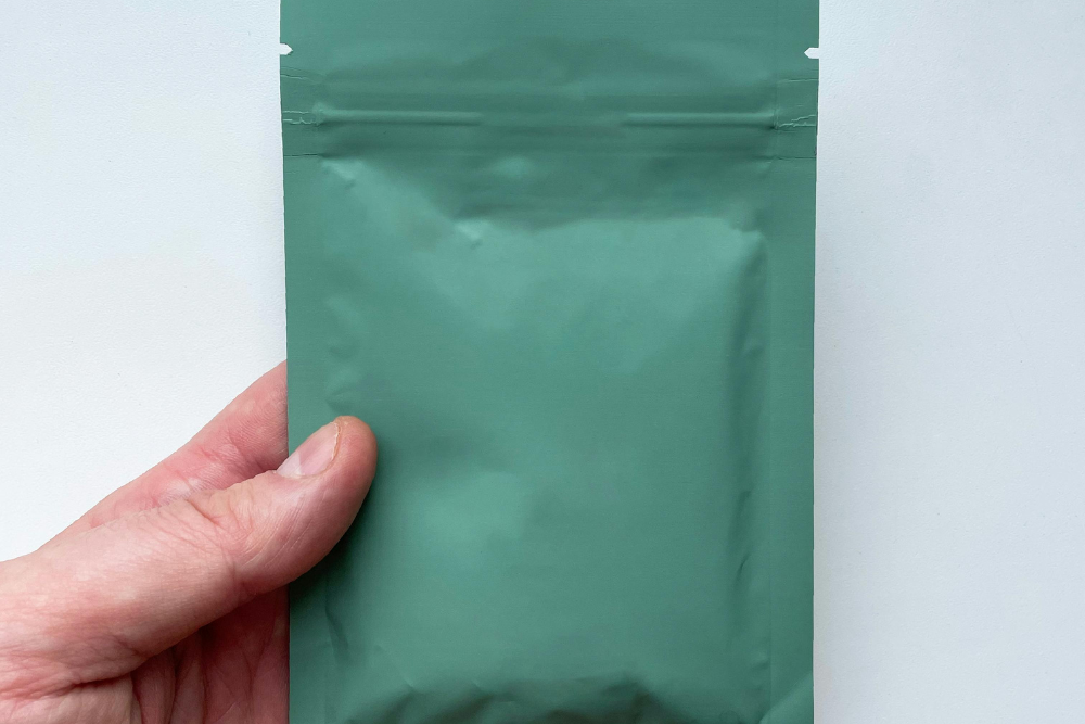 A hand holding a green, flat bag sample from RubeeFlex Packaging